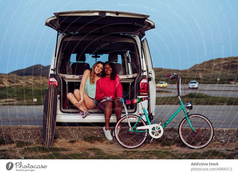 Fröhliche Frauen sitzen auf dem Kofferraum eines Lieferwagens Sitzen Essen Popkorn Wohnwagen Auto Reise Ausflug Transport Urlaub Abenteuer reisen Sommer