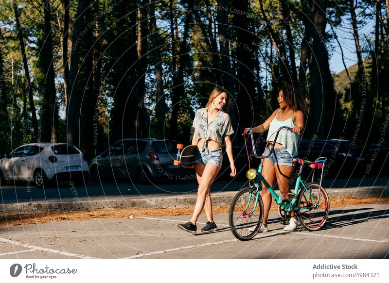 Freundinnen gehen auf der Straße und halten Skateboard und Fahrrad Beteiligung Großstadt Lachen Fröhlichkeit horizontal Lächeln laufen Holzplatte genießen 20s