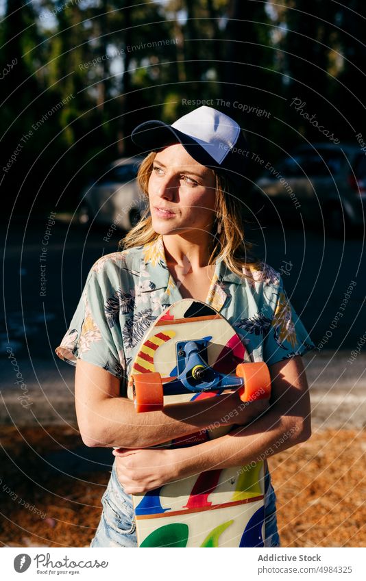 Skater, der im Freien wegschaut und ein Skateboard hält Frau Mode eine Kaukasier Skateboarderin Lifestyle cool Mädchen urban Straße Skateboarding Freizeit