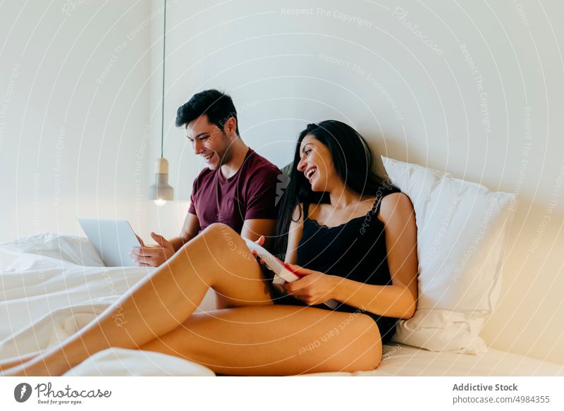 Ehepaar mit Buch und Laptop auf dem Bett im Schlafzimmer liegend Paar Frau Mann Leinen benutzend Raum Lautstärke lesen jung weiß Lügen Decke Browsen Gerät