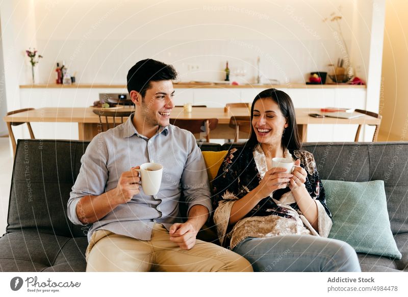 Glückliches Paar mit Tasse und Teller auf Sofa im Zimmer Raum hispanisch Küche Becher Kanapee heiter Lächeln Frau Mann jung attraktiv Getränk trinken Komfort