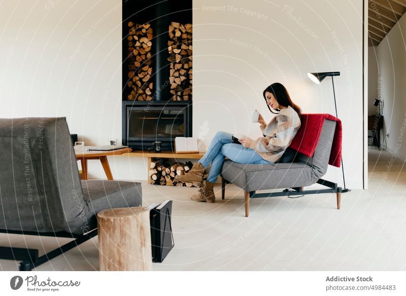 Junge Frau sitzt auf einem Sessel mit einem Buch in der Nähe des Kamins und des Fensters im Zimmer Armsessel Feuerstelle hispanisch Raum Dame Lautstärke