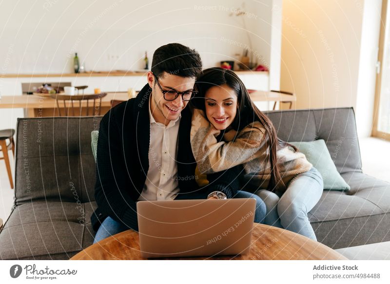 Mann benutzt Laptop in der Nähe einer glücklichen Frau auf dem Sofa Paar benutzend Glück hispanisch Tippen Brille Kanapee jung attraktiv Raum Gerät Apparatur