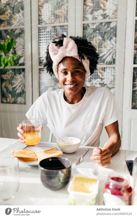 Glückliche ethnische Frau, die beim Frühstück einen Saft genießt Morgen heimwärts Lächeln Tisch Freude trinken Getränk sich[Akk] entspannen Lifestyle lässig