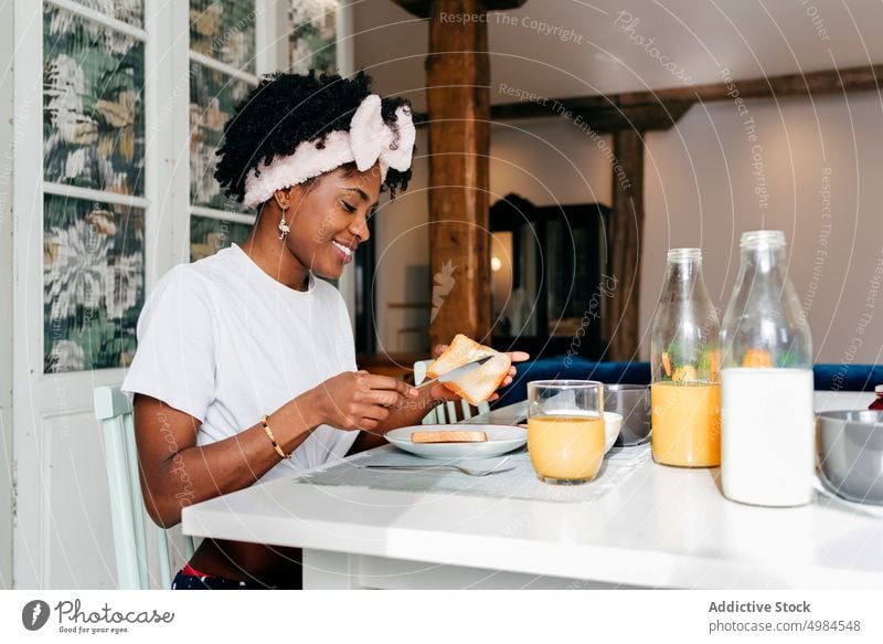 Schwarzes Mädchen, das beim Frühstück Butter auf einen Toast schmiert Frau heimwärts Lächeln Brot Zuprosten ethnisch Morgen jung Gesundheit Müsli Lebensmittel