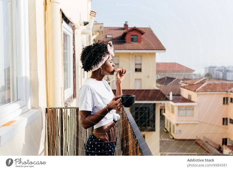 Schwarze Frau beim Frühstück auf dem Balkon trinken Zuprosten Appartement ethnisch Becher schlürfen essen schlank ruhen sich[Akk] entspannen Lifestyle Straße