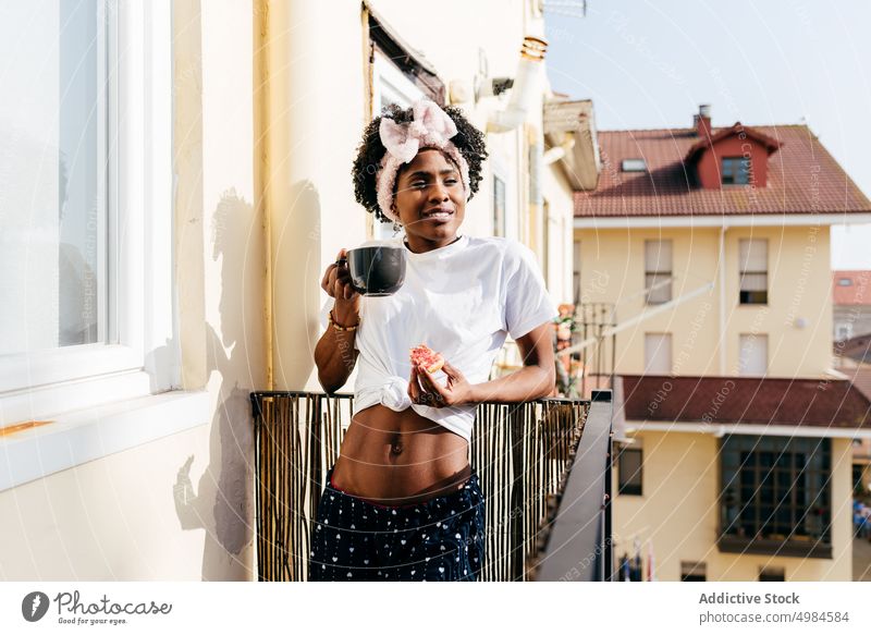 Schwarze Frau beim Frühstück auf dem Balkon trinken Zuprosten Appartement ethnisch Becher schlürfen essen schlank ruhen sich[Akk] entspannen Lifestyle Straße
