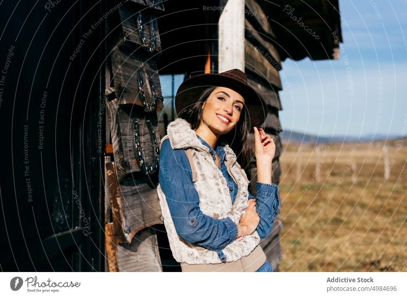 Stilvolle Frau mit Hut auf einer Ranch selbstbewusst heiter Haus Veranda Cowgirl Weste brünett Sonnenlicht attraktiv lässig Lifestyle Schönheit trendy Model
