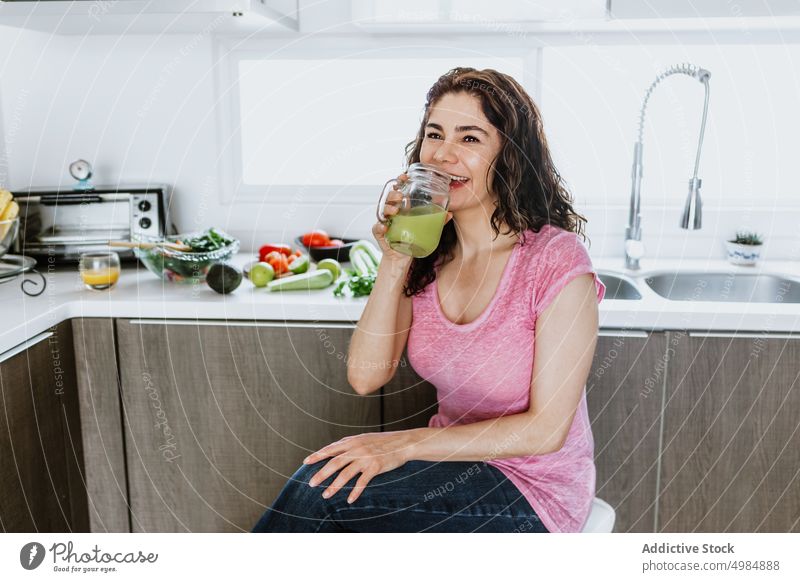 Glückliche Frau sitzt in der Küche und trinkt einen gesunden grünen Smoothie trinken Saft Entzug Gesundheit Bestandteil Gemüse positiv heiter