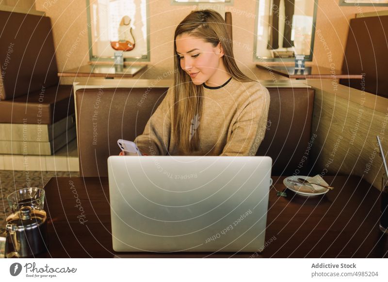 Lächelnder Freiberufler, der in einem Café mit seinem Smartphone chattet Frau freiberuflich Textnachricht Laptop trinken Kaffee Freude Tisch Gerät Apparatur