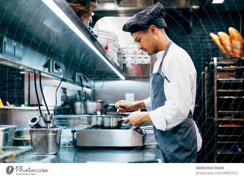 Mann kocht in moderner Küche Koch Küchenchef Abfertigungsschalter Restaurant Lebensmittel professionell Uniform Vorrichtung rostfrei Beruf Design Ansicht
