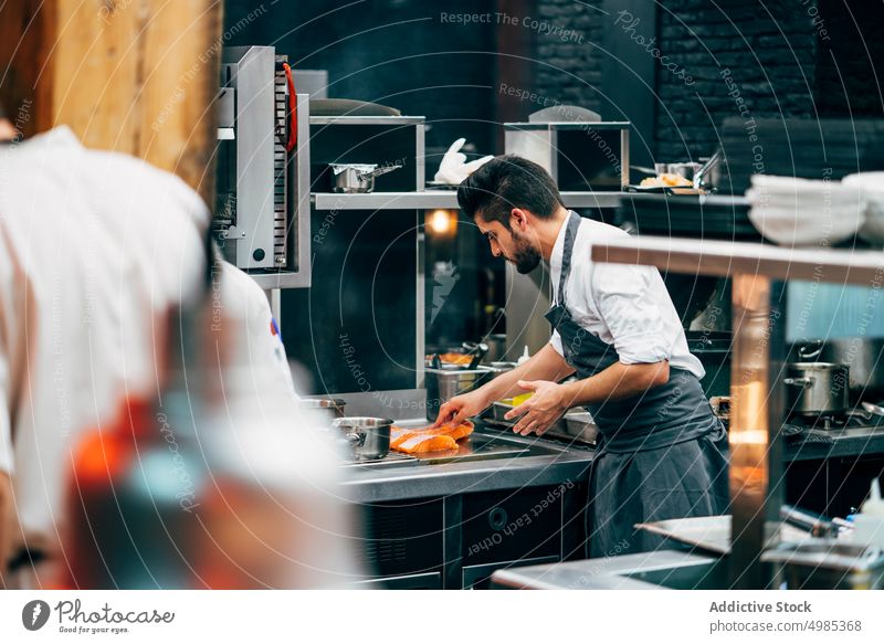 Mann kocht Lachs in einer modernen Küche Koch Küchenchef Abfertigungsschalter Restaurant Lebensmittel professionell Uniform Vorrichtung rostfrei Beruf Design