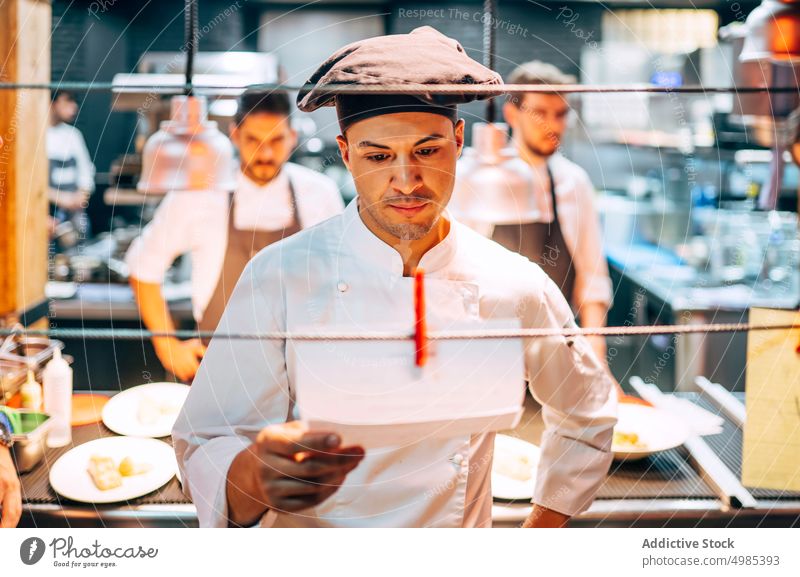 Mann liest Bestellungen auf Papier in der Küche Küchenchef lesen Orden List kulinarisch Restaurant Personal Speisekarte professionell Job Mahlzeit