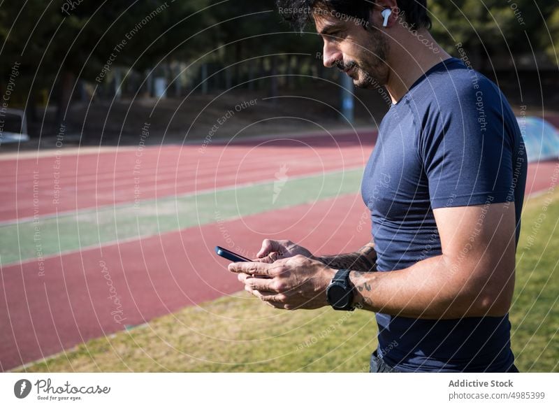 Ethnischer Sportler benutzt Smartphone im Stadion Browsen Läufer Sommer benutzend Training Surfen männlich ethnisch hispanisch Mann Mobile Telefon Anschluss