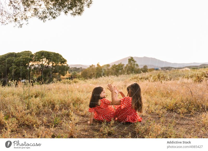 Zwei glückliche kleine Schwestern sitzen auf einer Wiese Mädchen Sommer Natur Sitzen Urlaub Glück sorgenfrei Freund Spaß rot Spielen Familie Kleid Feld