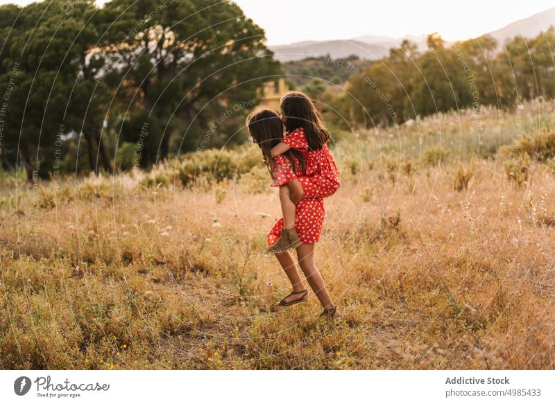 Lächelndes Mädchen trägt Schwester auf dem Rücken in einem Feld Huckepack Sommer Natur Mitfahrgelegenheit führen Urlaub Glück sorgenfrei Freund Spaß Wiese rot