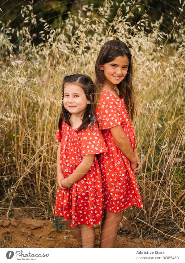 Lächelnde Mädchen stehen auf einer Wiese mit hohem Gras Schwester Sommer Glück Natur Feld Kindheit rotes Kleid Urlaub Ausdruck Spaß Freund ähnlich Familie