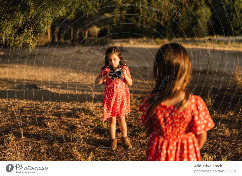 Mädchen, das seine kleine Schwester auf einer Wiese fotografiert Freundschaft fotografierend Sommer Feld Natur Fotokamera Fotografie Glück schön