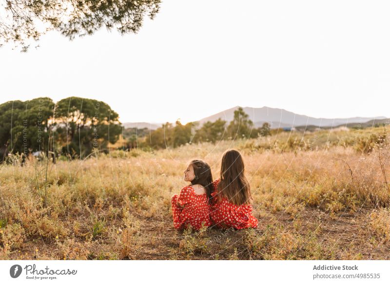 Zwei glückliche kleine Schwestern sitzen auf einer Wiese Mädchen Sommer Natur Sitzen Urlaub Glück sorgenfrei Freund Spaß rot Spielen Familie Kleid Feld