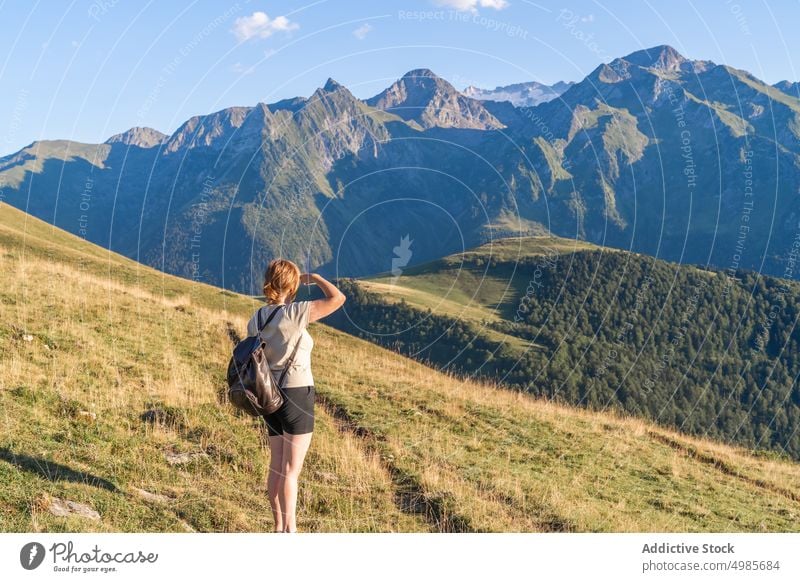 Unerkennbare Frau steht auf einem grasbewachsenen Hügel vor einem felsigen Gebirge Berge u. Gebirge Hochland Berghang bewundern malerisch schwer Ambitus