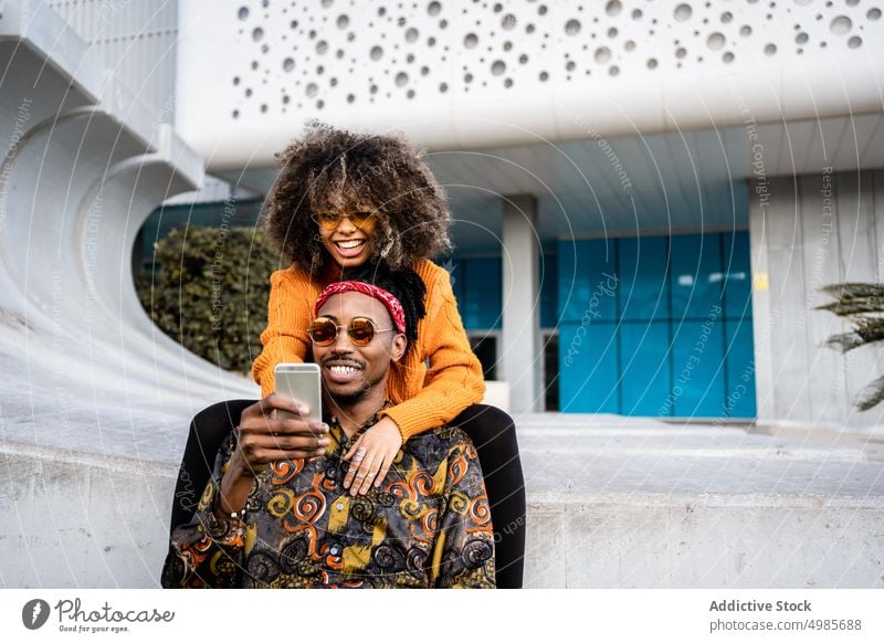Lachende stilvolle ethnische Paar unter Selfie auf Bank trendy Smartphone urban benutzend teilen Stil schwarz Afroamerikaner cool Streetstyle heiter Glück