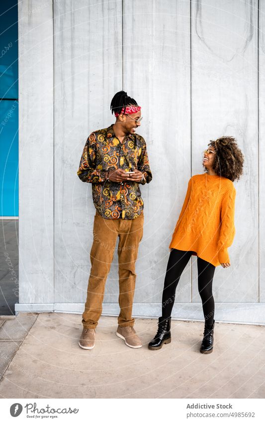 Stilvolles schwarzes Paar benutzt Smartphone im Sonnenlicht trendy farbenfroh urban Glück heiter ethnisch Liebe Afroamerikaner Lachen Afro-Look Rastalocken