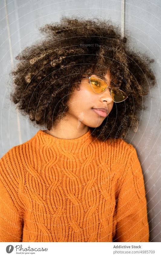 Trendy schwarze Frau in hellem Pullover auf der Straße farbenfroh Streetstyle ethnisch Afroamerikaner modern cool schlank Sonnenbrille charmant Frisur Afro-Look