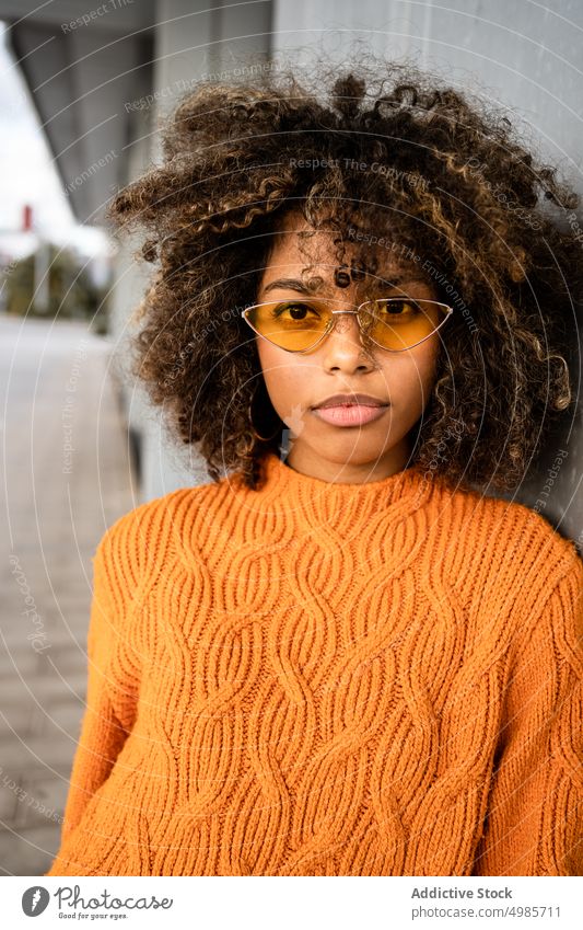 Trendy schwarze Frau in hellem Pullover auf der Straße farbenfroh Streetstyle ethnisch Afroamerikaner modern cool schlank Sonnenbrille charmant Frisur Afro-Look