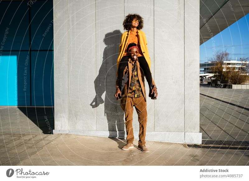 Cooler Mann mit Freundin auf den Schultern in der Stadt Paar Streetstyle führen trendy urban Mode Straße hoch farbenfroh ethnisch schwarz Afroamerikaner Stil