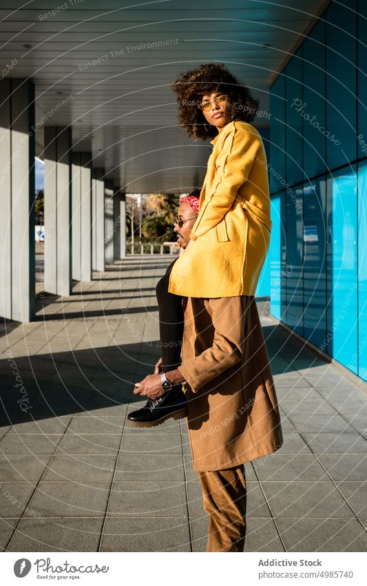 Cooler Mann mit Freundin auf den Schultern in der Stadt Paar Streetstyle führen trendy urban Mode Straße hoch farbenfroh ethnisch schwarz Afroamerikaner Stil