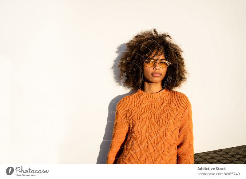 Trendy schwarze Frau in hellem Pullover auf der Straße farbenfroh Streetstyle heiter ethnisch Afroamerikaner modern cool schlank Sonnenbrille charmant Frisur