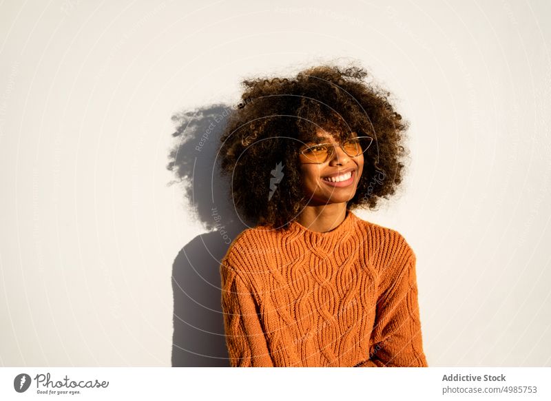 Trendy schwarze Frau in hellem Pullover auf der Straße farbenfroh Streetstyle heiter ethnisch Afroamerikaner modern cool schlank Sonnenbrille charmant Frisur
