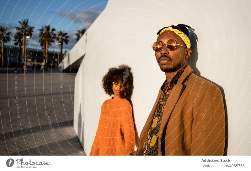 Moderner schwarzer Mann und Frau vor weißer Wand im Sonnenuntergang Paar Stil Großstadt ethnisch Zusammensein Streetstyle cool Afroamerikaner Zeitgenosse