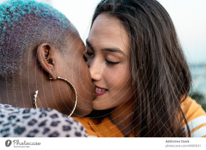 Multirassisches lesbisches Paar sitzt im Freien eng zusammen Nähe Partnerschaft Bonden Liebe Kuss Küssen lgbt Homosexualität Zusammensein jung multiethnisch