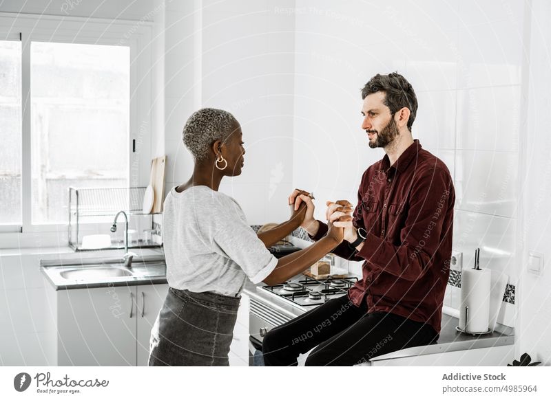 Vergnügtes multiethnisches Liebespaar hält sich in der Küche an den Händen Paar Umarmung kuscheln sitzen Kabinett heimwärts Partnerschaft Lächeln Zuneigung