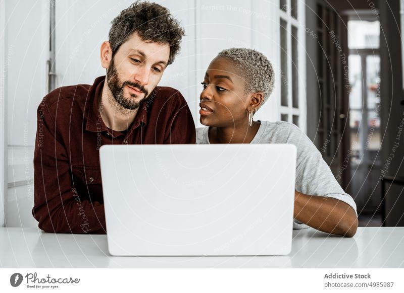 Intelligentes multiethnisches Paar nutzt Gadgets zu Hause benutzend Apparatur Laptop Gerät beschäftigt Süchtige digital sitzen Tisch Browsen zuschauen heimwärts