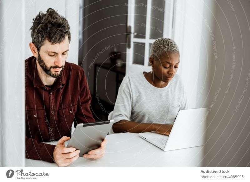 Intelligentes multiethnisches Paar nutzt Gadgets zu Hause benutzend Apparatur Laptop Gerät beschäftigt Süchtige digital sitzen Tisch Browsen zuschauen heimwärts