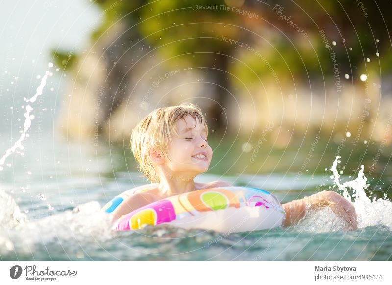 Kleiner Junge schwimmt mit buntem Schwimmring im Meer an einem sonnigen Sommertag. Nettes Kind spielt am Strand. Familie und Kinder Resort Urlaub während der Sommerferien.