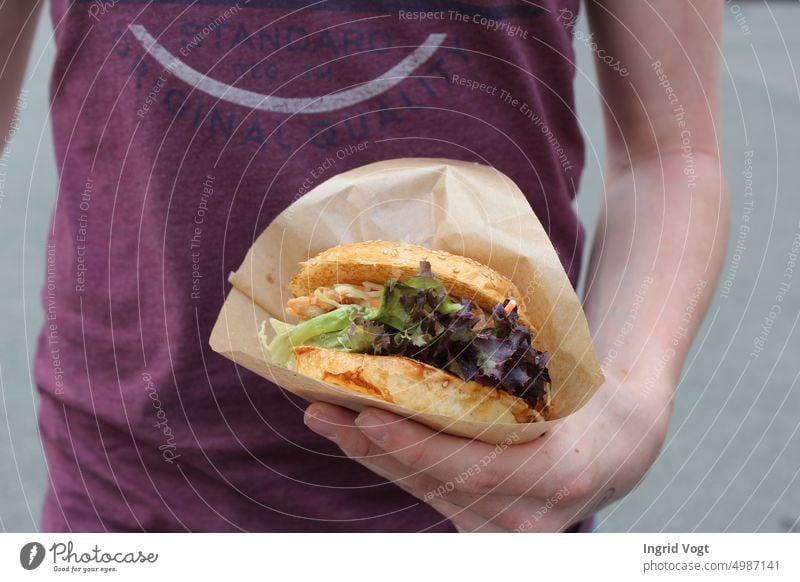 Junger Mann hält Burger in der Hand Hamburger Streetfood Essen Fast Food Salat Linkshänder
