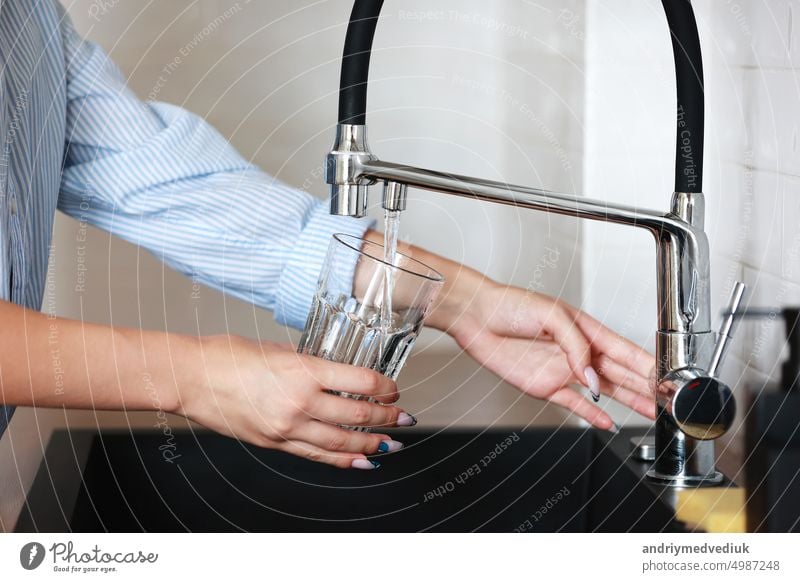 Frau füllt Trinkglas mit Leitungswasser in der Küche. Konzept der sauberen Trinkwasser Leitungswasser zu Hause. Pouring frisches Getränk. Konzept zur Überprüfung der Wasserqualität. Das Konzept der Einsparung, Probleme mit Wasser