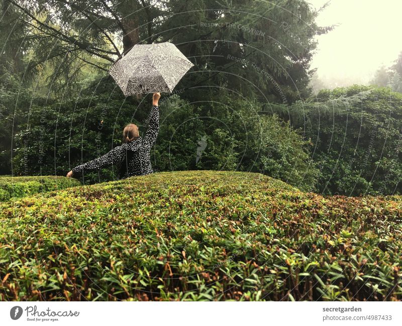 [HH unnamed road] Da ist was im Busch.... Park Regen Schirm Frau Hecke grün Garten hüpfen Freude nass Regenjacke Außenaufnahme schlechtes Wetter Natur Farbfoto