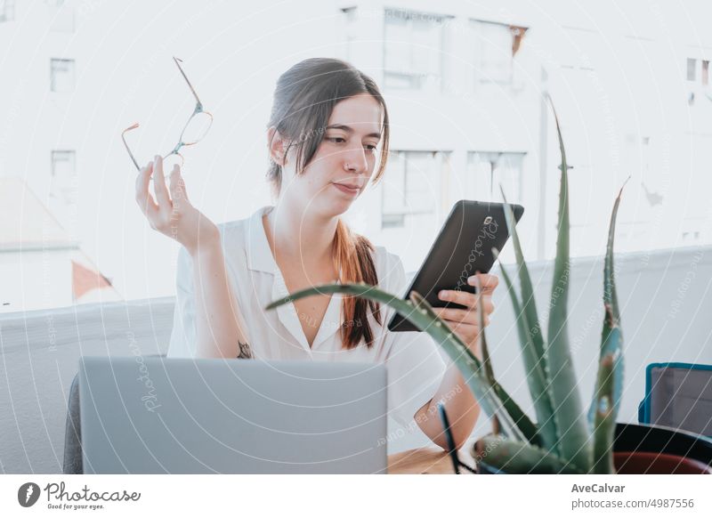 Junge Geschäftsfrau, die ihr Tablet überprüft und eine Brille auf einer Terrasse im Büro während eines sonnigen Tages hält Computer Frau Laptop eine Person