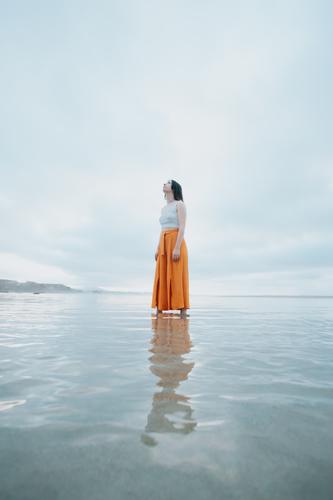 Frau steht auf trendigen Kleidern am Strand, während sie sich im Wasser spiegelt sorgenfrei energetisch Freiheit Freude positiv aktiv Spaß Glück Meer Sonne jung