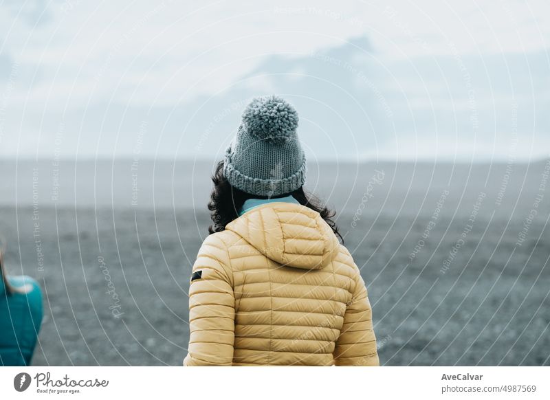 Frau auf dem schwarzen Sandstrand in Island, Winterkleidung.Shot von hinten.Travel to iceland Konzept. Felsen wüst Person Insel Meer Süden allein Gleichgewicht