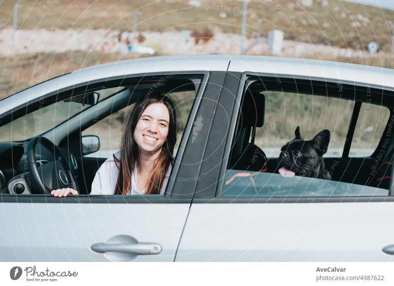 Junge Frau und Hund französische Bulldogge, die sich vor einem Spaziergang fröhlich aus den Autofenstern zeigen. Lustiges Bild Haustier Fenster Porträt Eckzahn