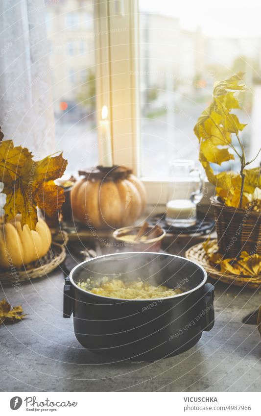 Gedämpfter Kochtopf mit Herbstgerichten auf dem Küchentisch mit Kürbissen am Fenster gedünstet Komfortnahrung Lifestyle Kerze Tisch lecker Mahlzeit Hintergrund