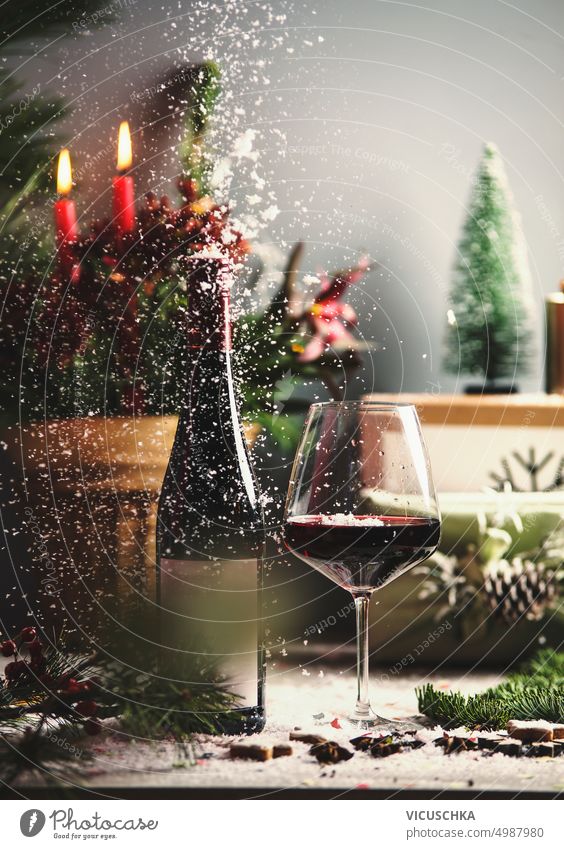 Weihnachten Rotwein Glas und Flasche auf dem Tisch mit Kerzen, Urlaub Dekorationen, Geschenk-Boxen und fallenden Schnee Weinglas Weinflasche Feiertag