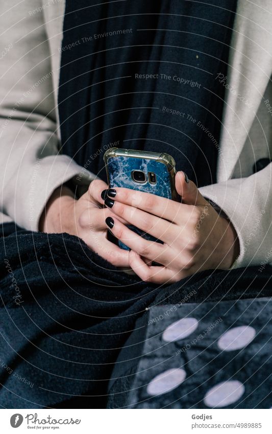 [HH Unnamed Road] Sitzende Frau hält Smartphone in ihrer Hand Handy Lifestyle Telefon sitzend lässig halten Hände schwarze Nägel Schal Mantel