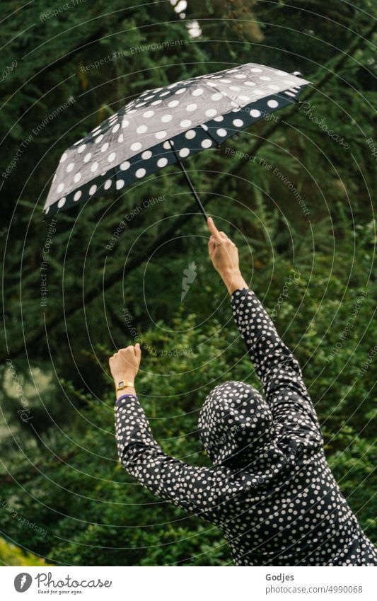 [HH Unnamed Road] Rückansicht einer Person mit gepunkteter Regenjacke und passendem Regenschirm. eine Person Frau im Freien Natur grün schwarz-weiß Farbfoto