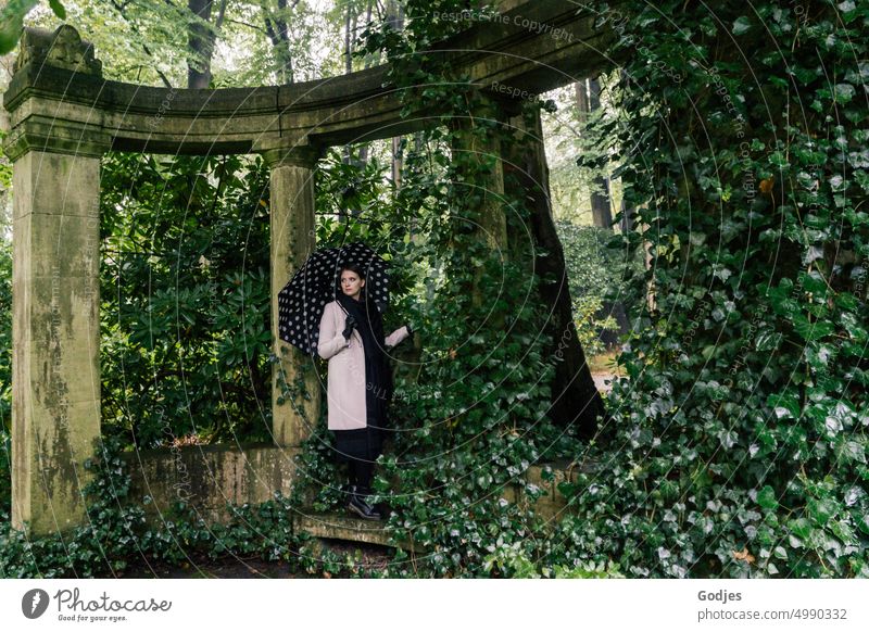 [HH Unnamed Road] Junge Frau mit Regenschirm steht in einem Säulenbogen, der mit Efeu bewachsen ist Blätterdach Grabmal Denkmal historisch Farbfoto